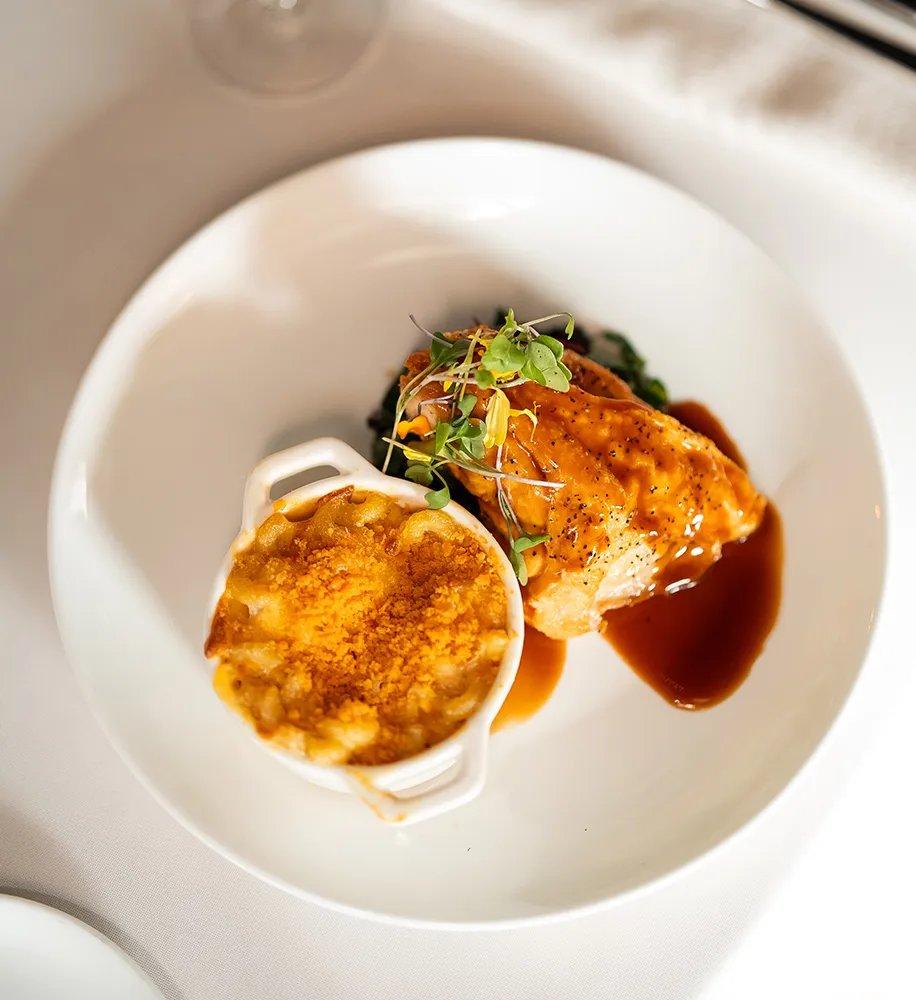 Glazed chicken breast with brown sauce served alongside baked mac and cheese topped with microgreens