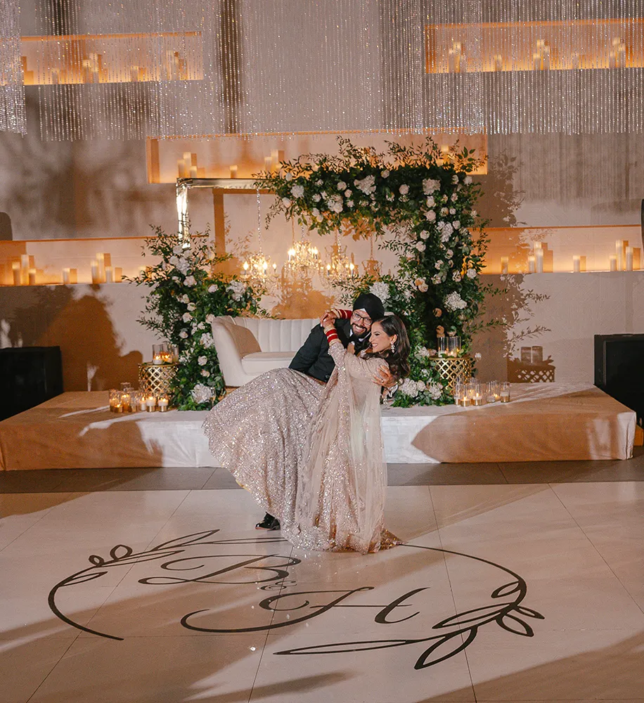 Couple sharing a dip on a monogrammed dance floor surrounded by candlelight and greenery