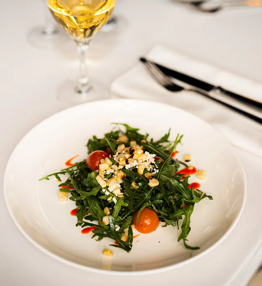 Arugula salad with cherry tomatoes, corn, and crumbled cheese served with a glass of white wine
