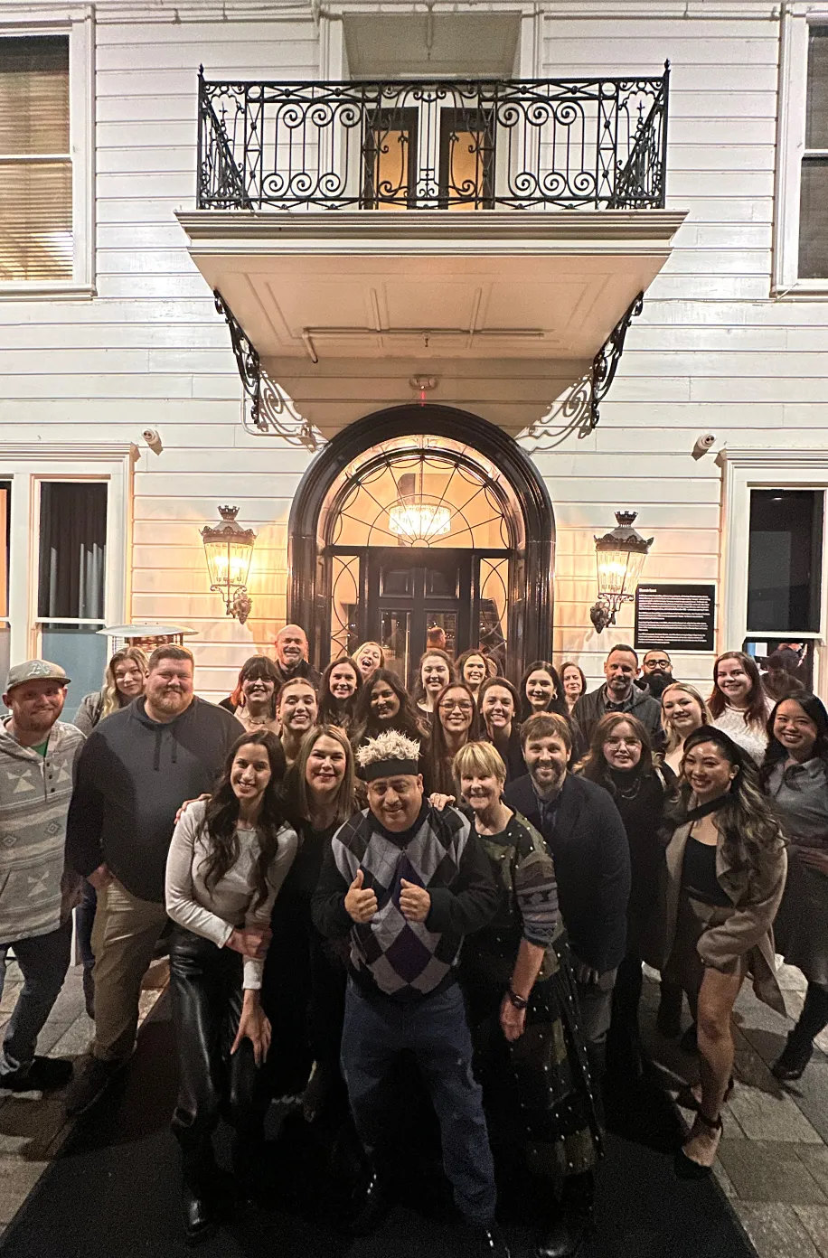 Team gathering on the front steps of a historic Victorian building in the evening