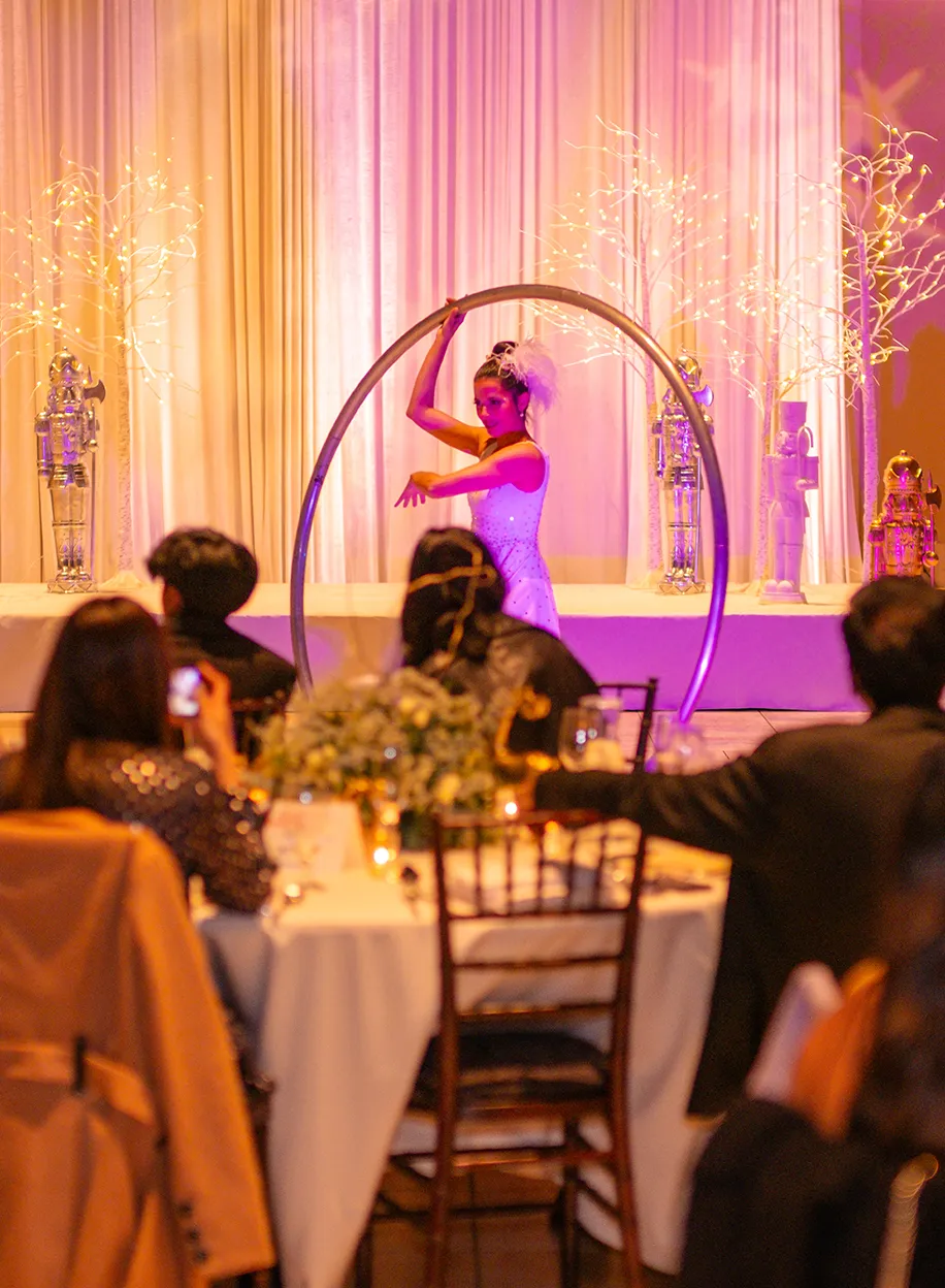 Acrobat performing inside a large metal hoop on stage while guests watch from candlelit dinner tables
