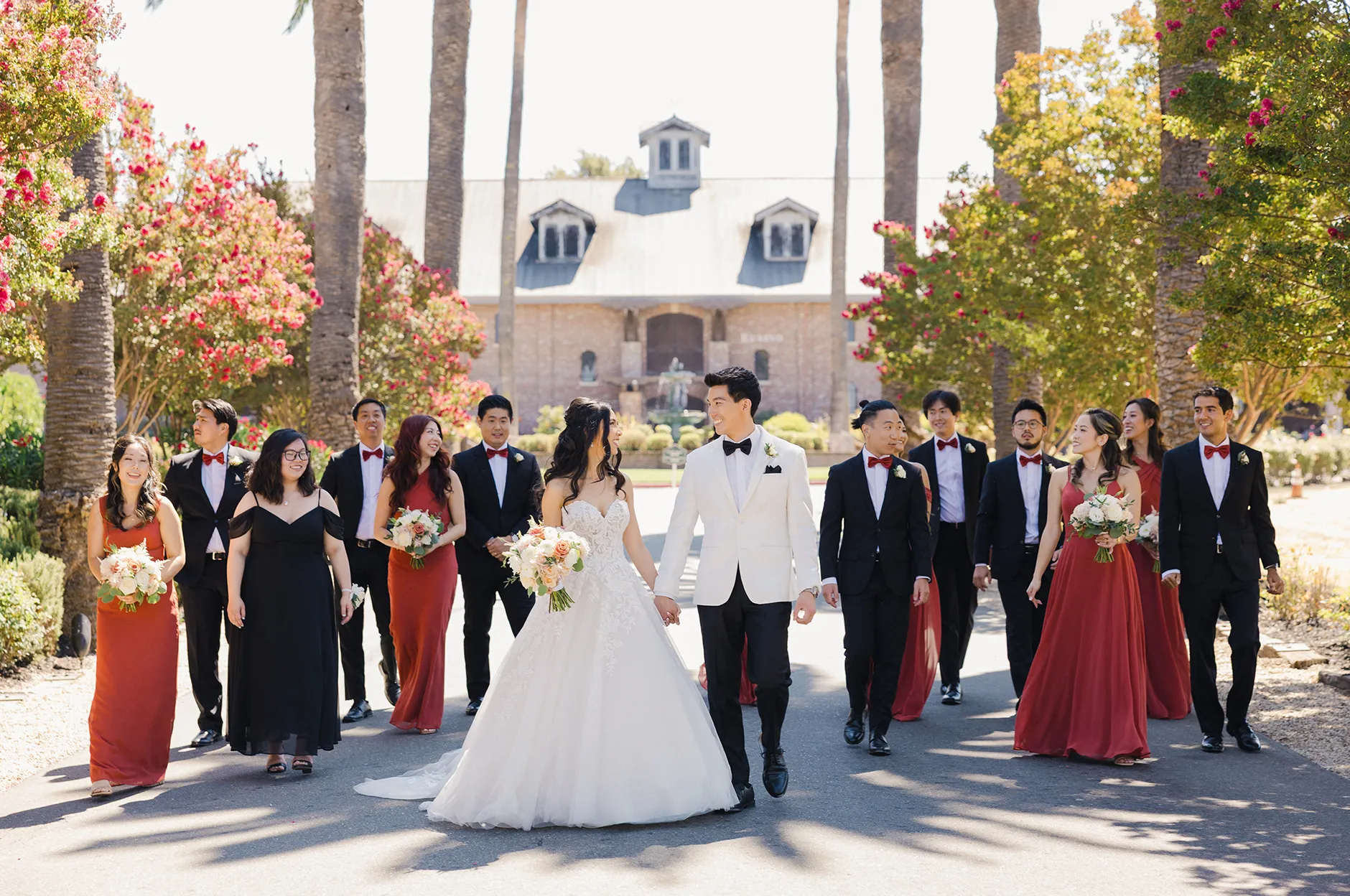 Wedding party in red and black walking together along a palm-lined path at the venue