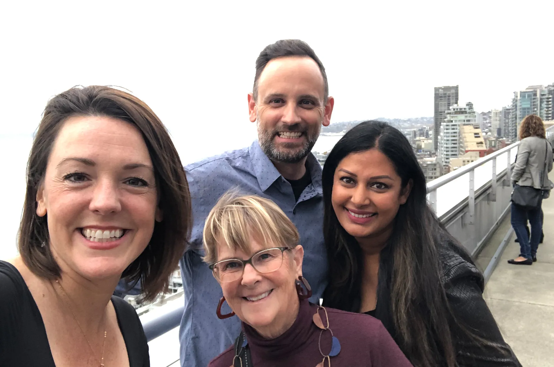 Four team members taking a selfie on a rooftop observation deck overlooking a city skyline