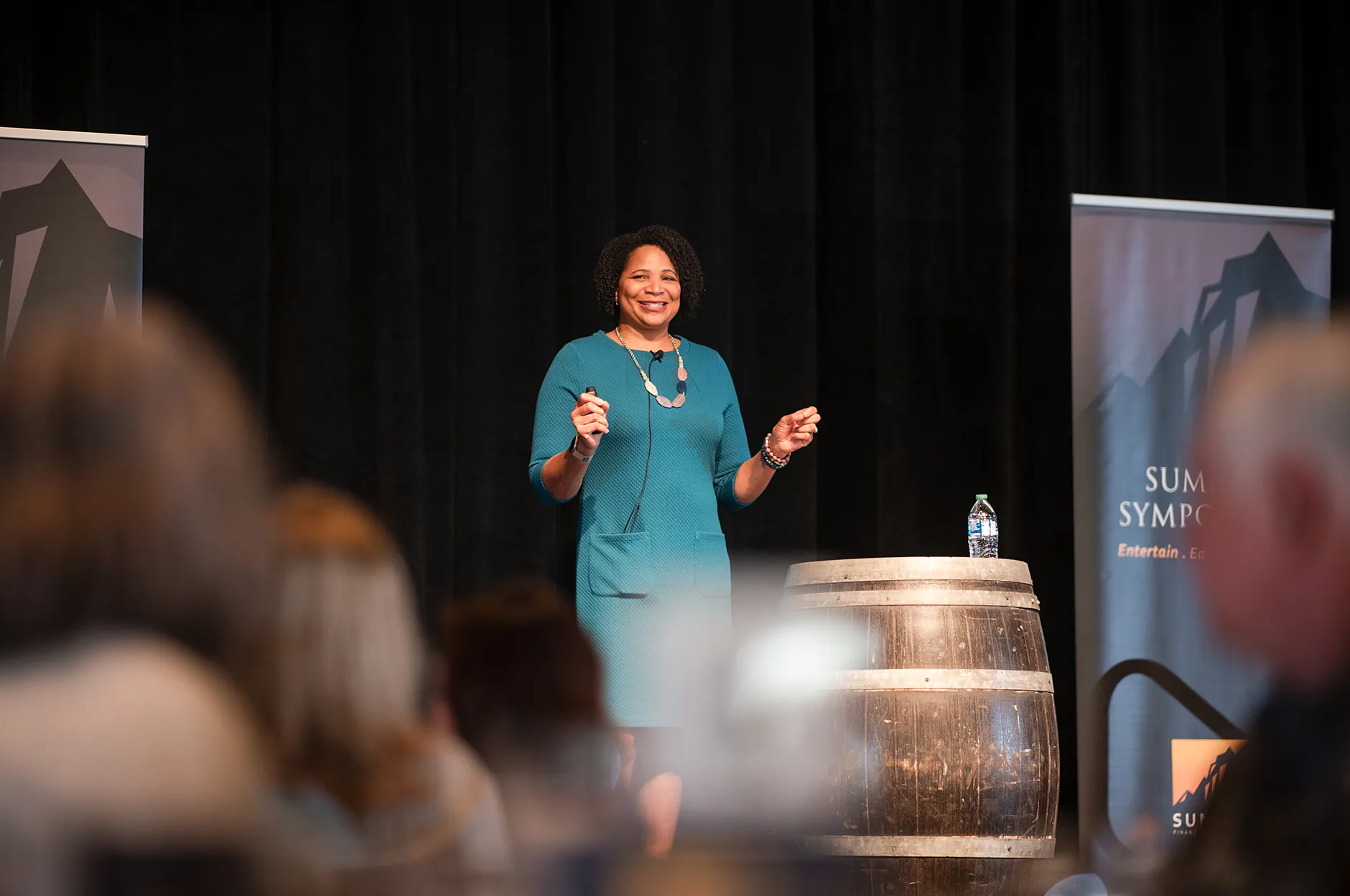 Keynote speaker addressing an audience from a stage with a wine barrel podium at a corporate symposium