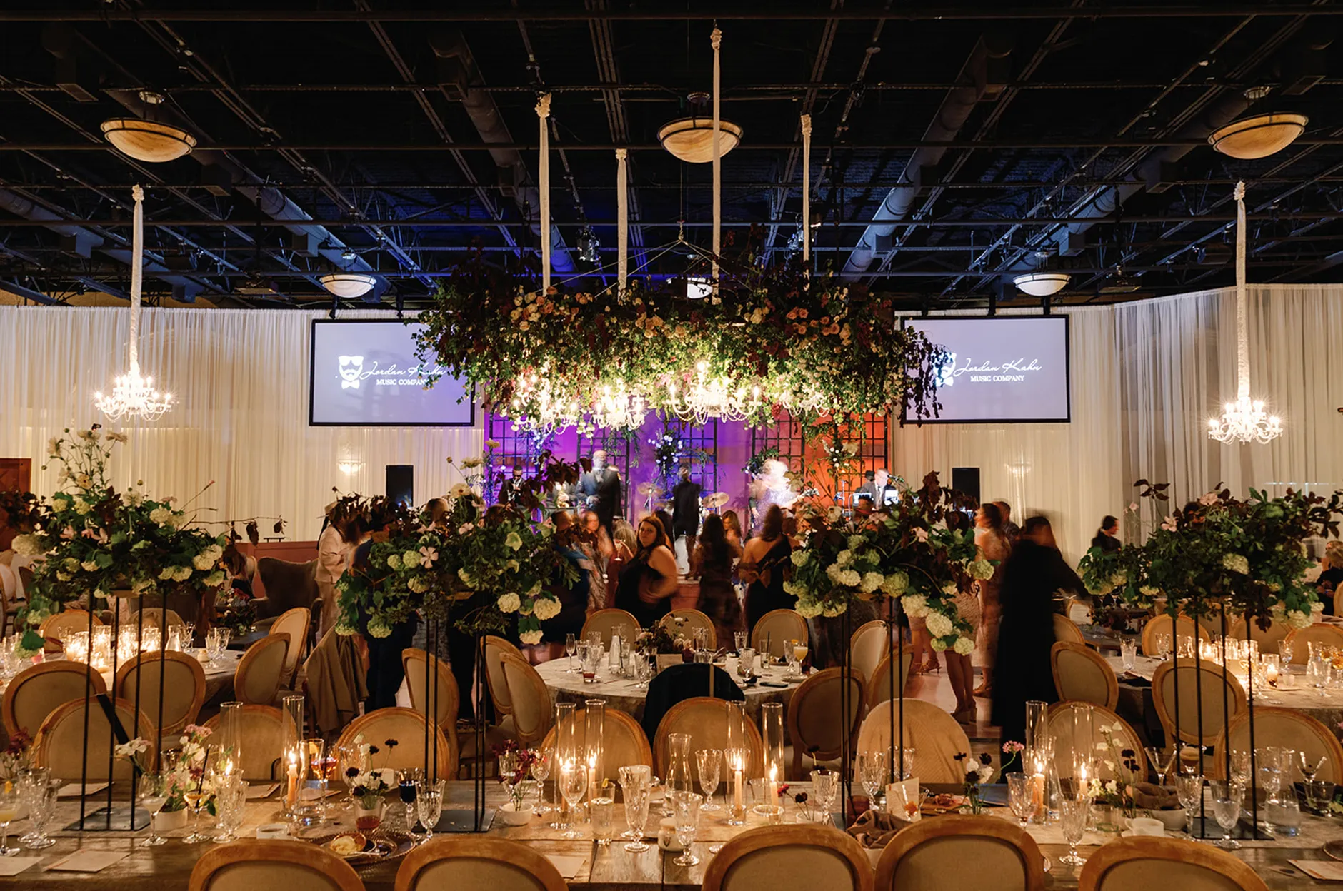 Guests mingling at a lavish evening gala with greenery centerpieces, hanging floral chandeliers, and candlelit tables