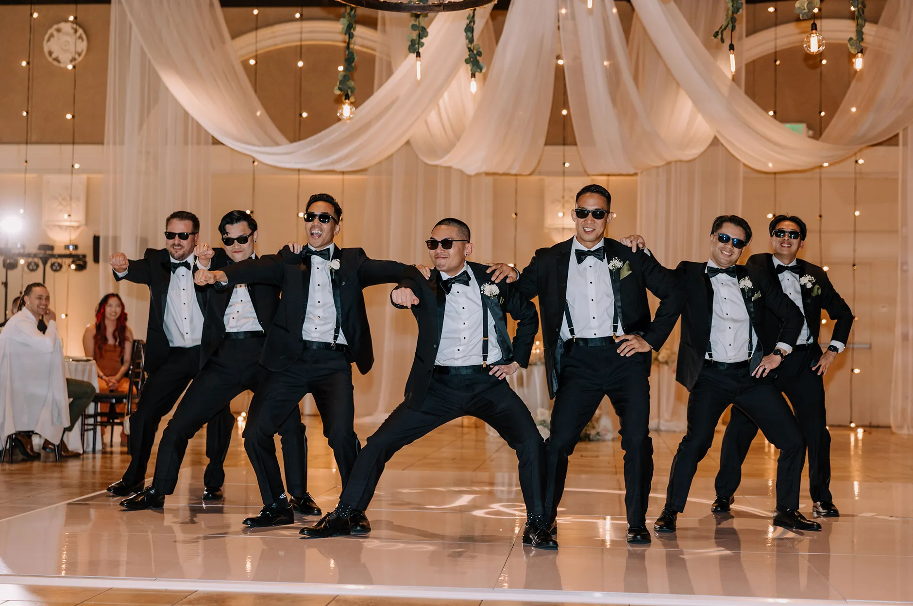 Groomsmen in matching tuxedos and sunglasses striking a choreographed pose on the dance floor