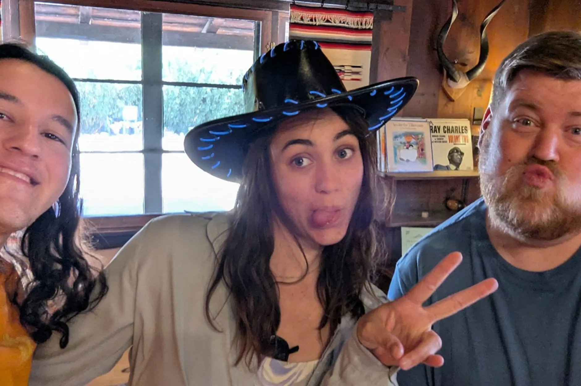 Three team members posing playfully in a rustic saloon with a cowboy hat and peace sign