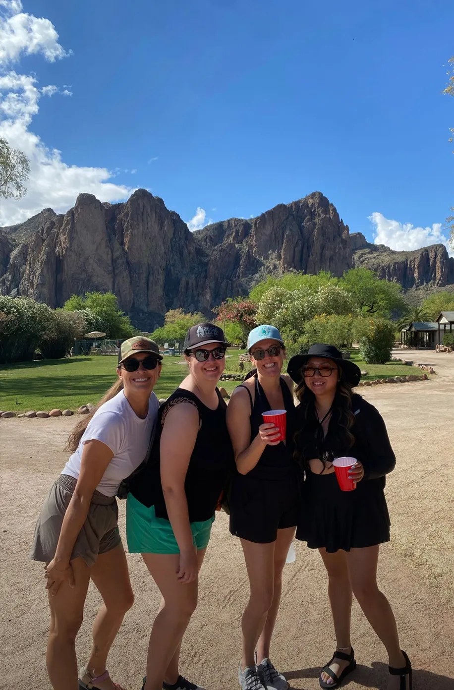 Four team members holding drinks and smiling together outdoors with desert mountains behind them