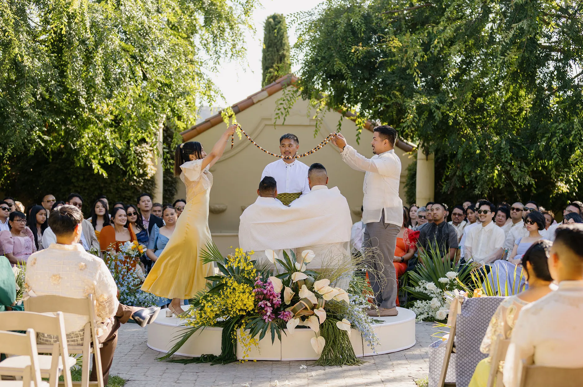 Outdoor wedding ceremony with the couple on a round platform surrounded by tropical florals and guests