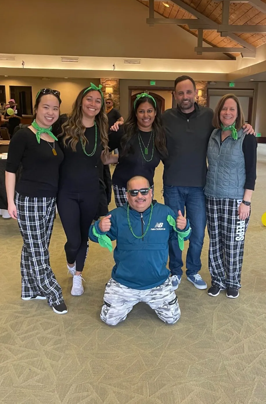 Six team members wearing matching green headbands and beads posing together in the venue lobby