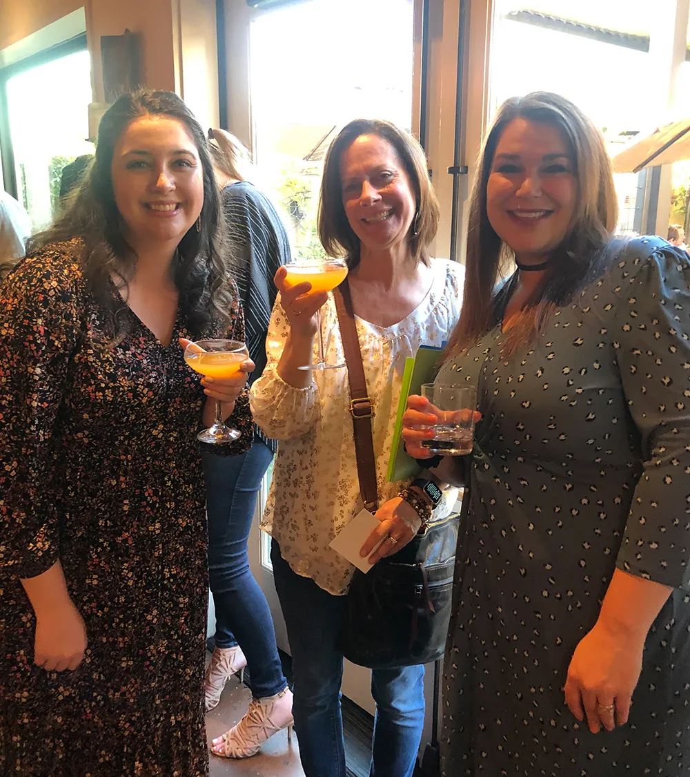 Three team members smiling and holding cocktails
