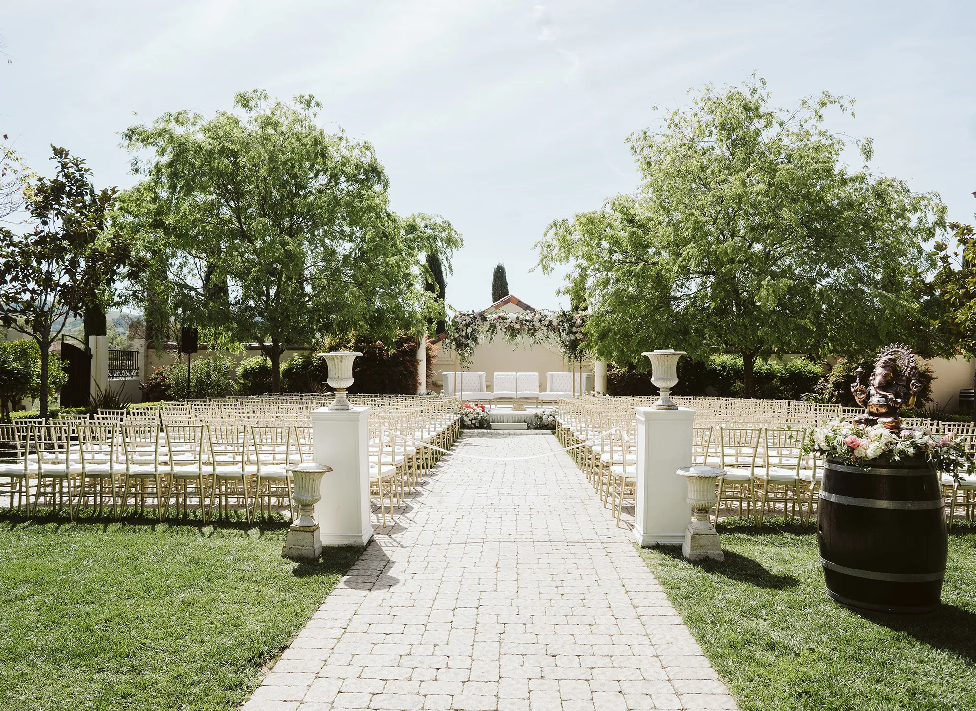 Sun Garden from the entrance with a brick walkway, white columns, gold chairs, urns, and a wine barrel with flowers