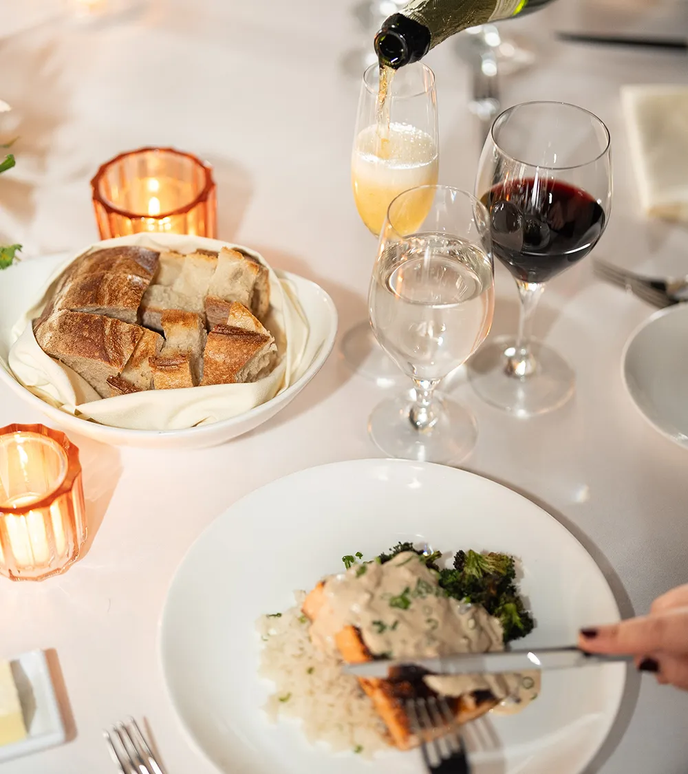 Champagne being poured at an elegantly set dinner table with artisan bread and wine