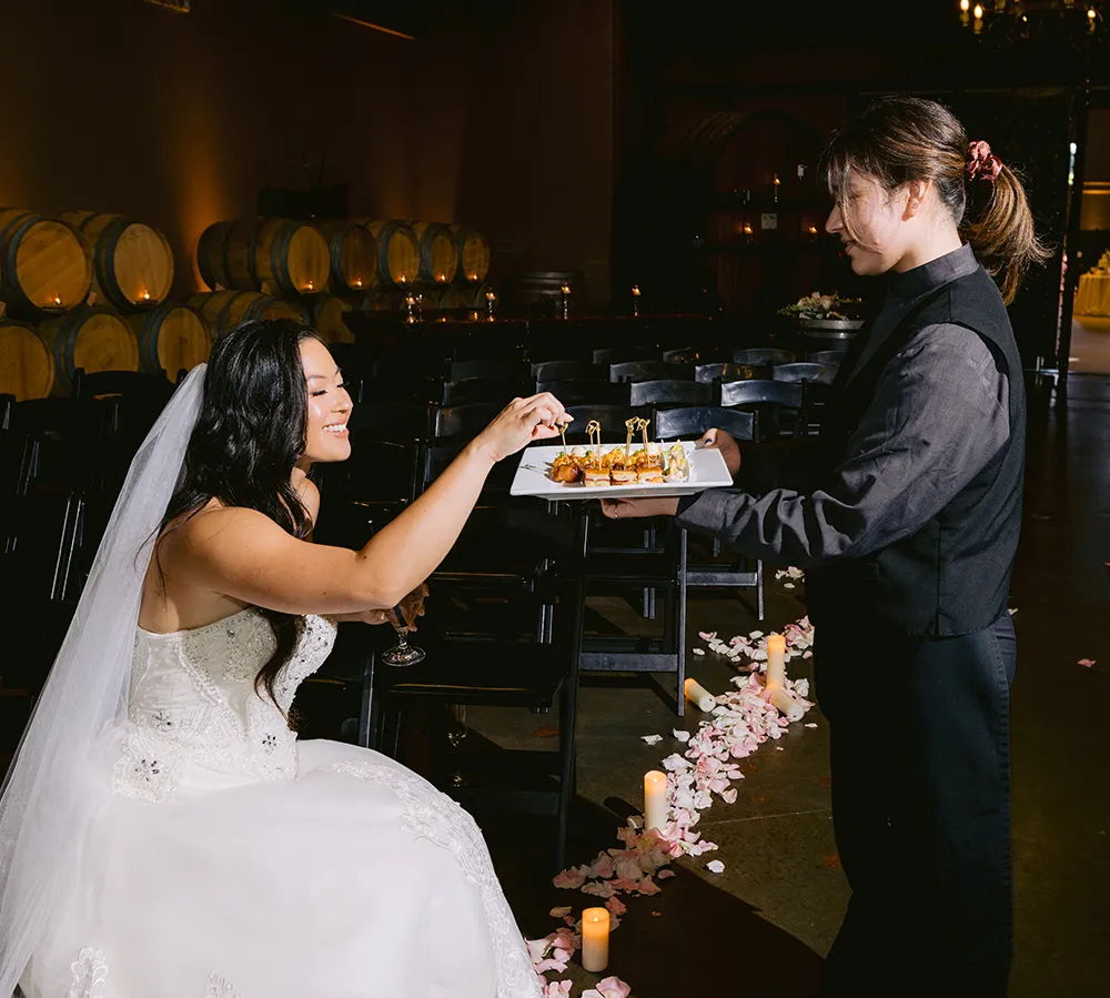 Banquet server presenting hors d'oeuvres to a bride in a candlelit wine barrel room