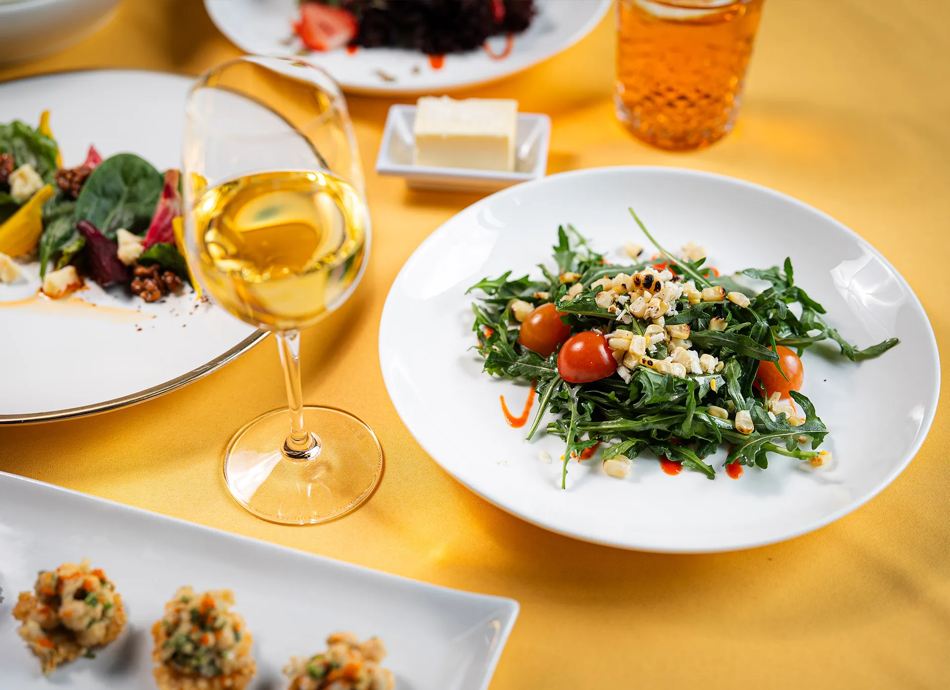 Arugula salad with cherry tomatoes alongside a glass of white wine on a golden tablecloth