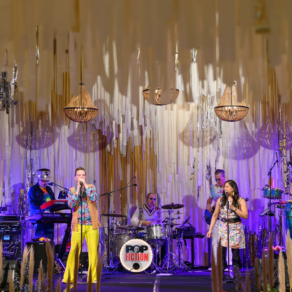Live band performing on stage beneath hanging ribbon and chandelier installations