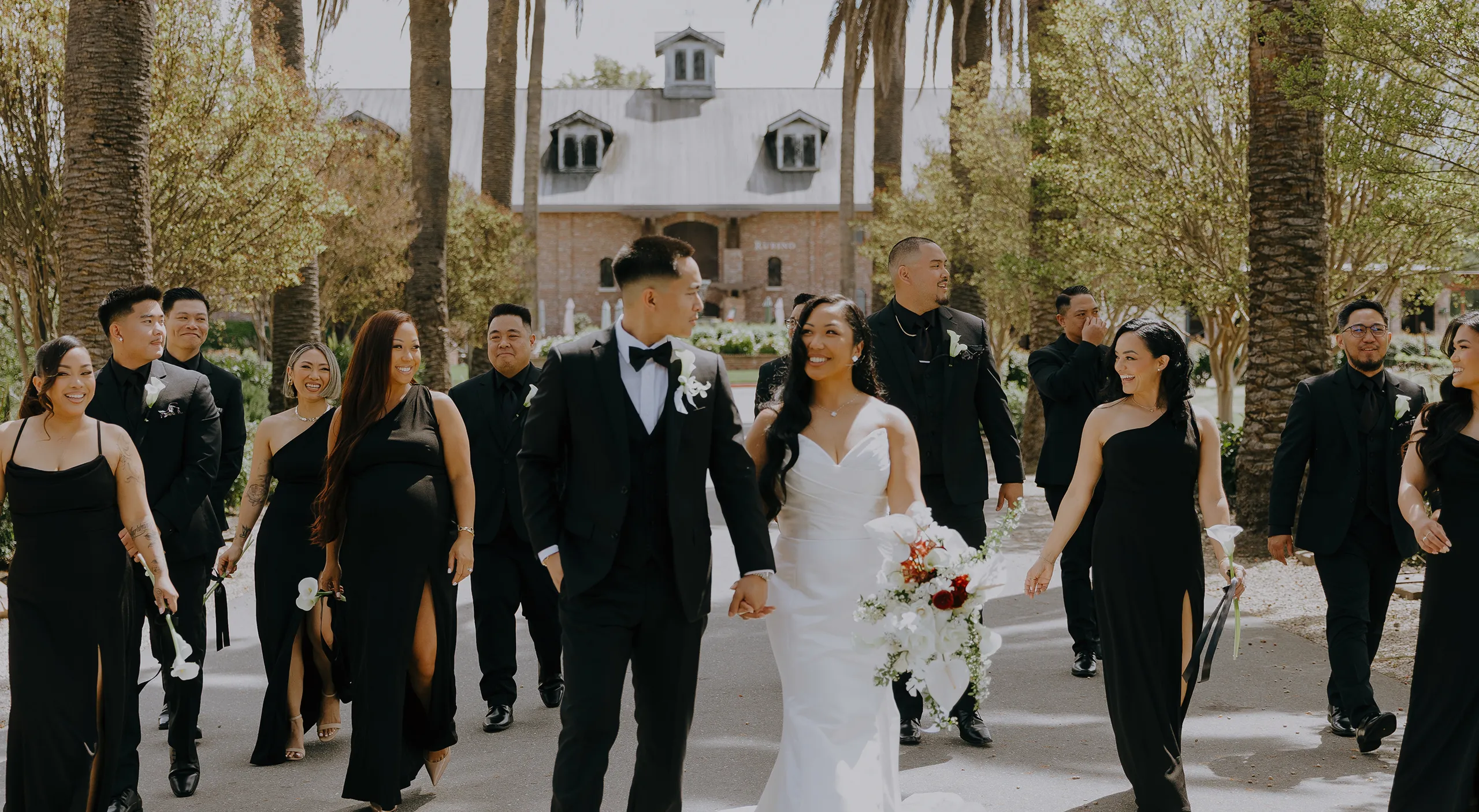 Bride and groom walking with their wedding party along a palm-lined path at the venue