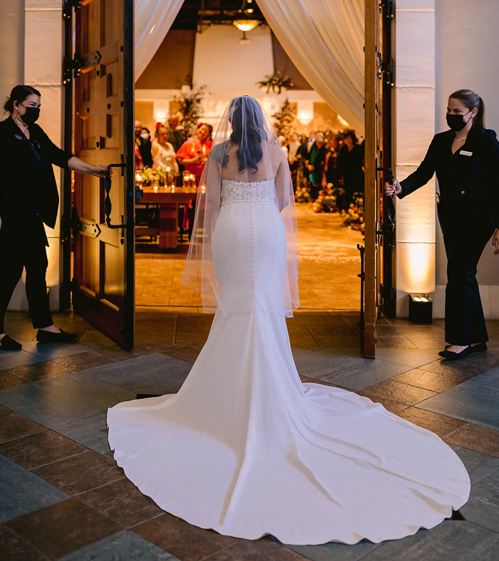 Bride making a grand entrance through open doors into her reception